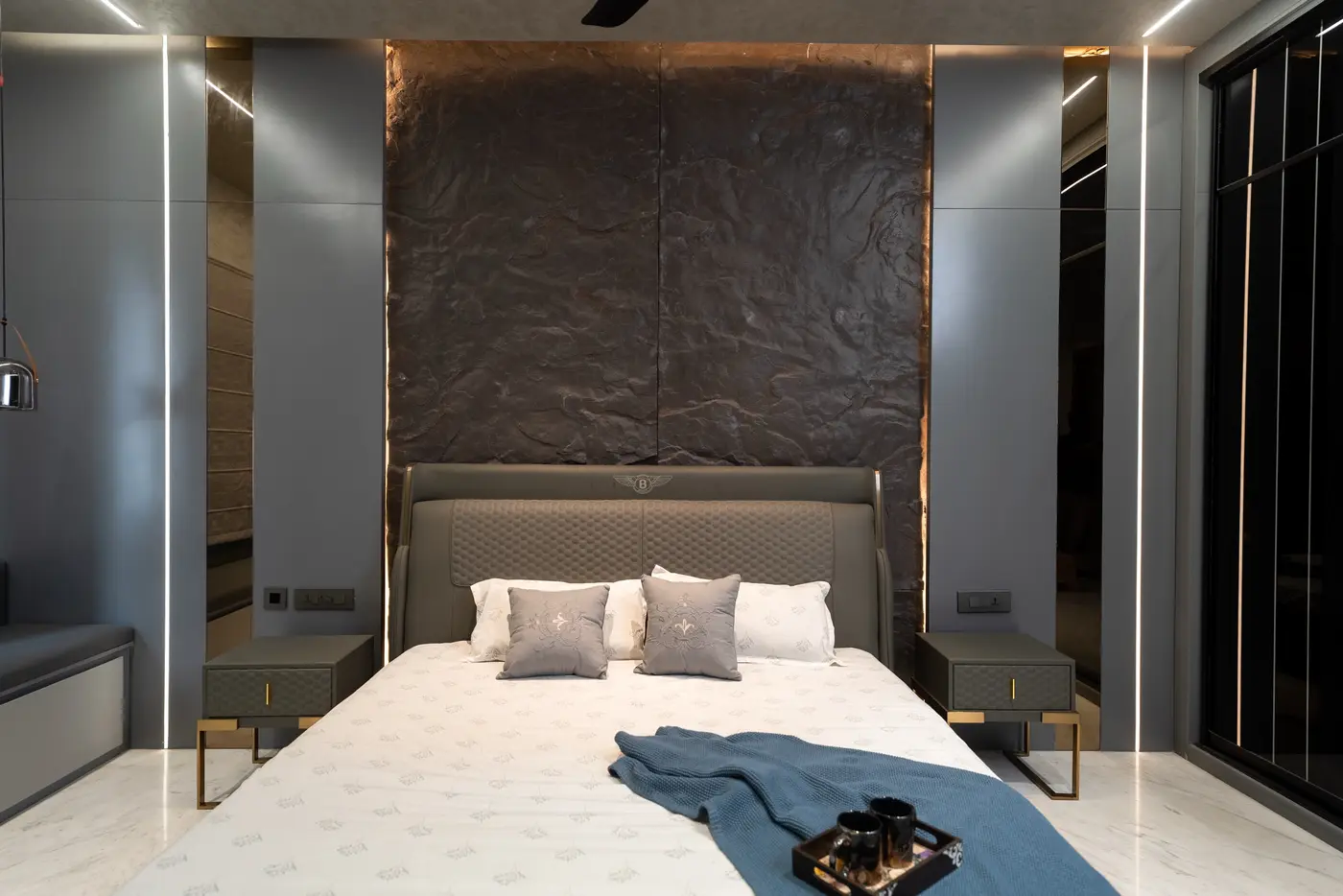 Bedroom with a textured stone feature wall, linear lights and switch panels placed beside the bedside tables