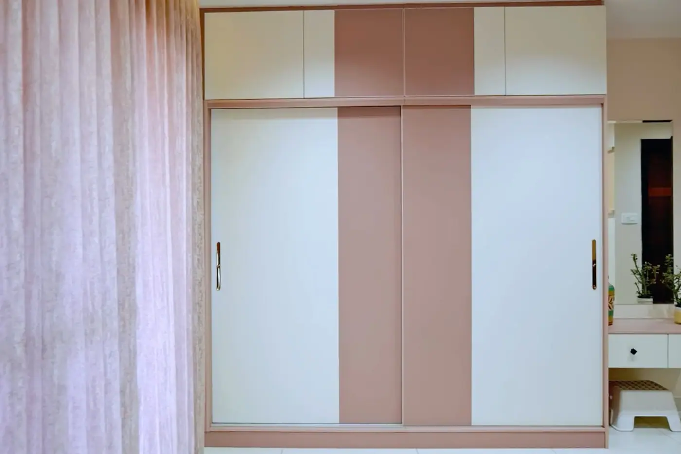 Bedroom wardrobe with white and blush laminate shutters and a loft above