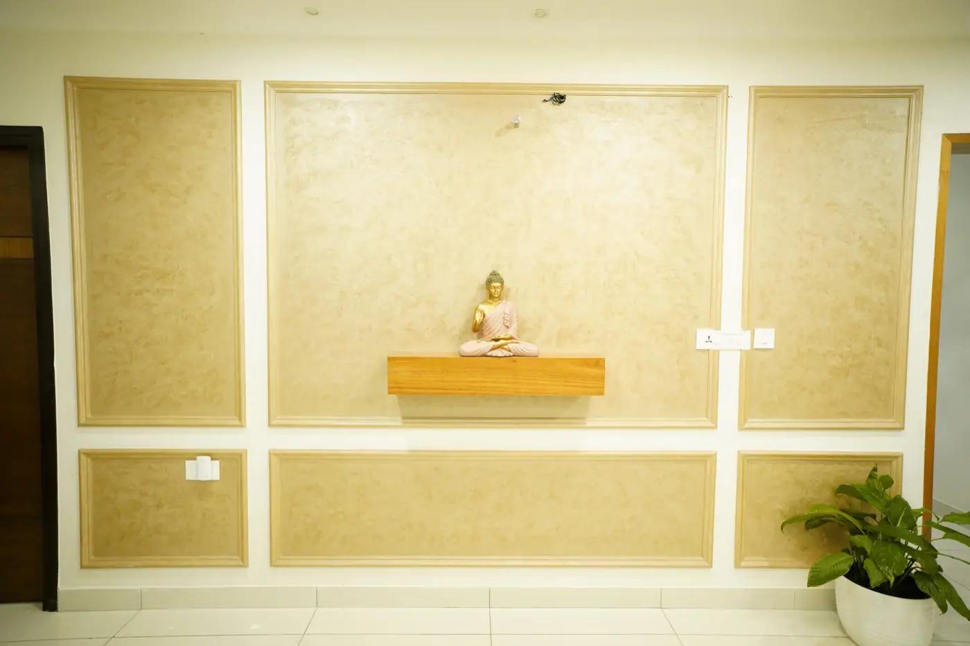 Textured gold-toned wall panel with framed inlays and a small floating shelf